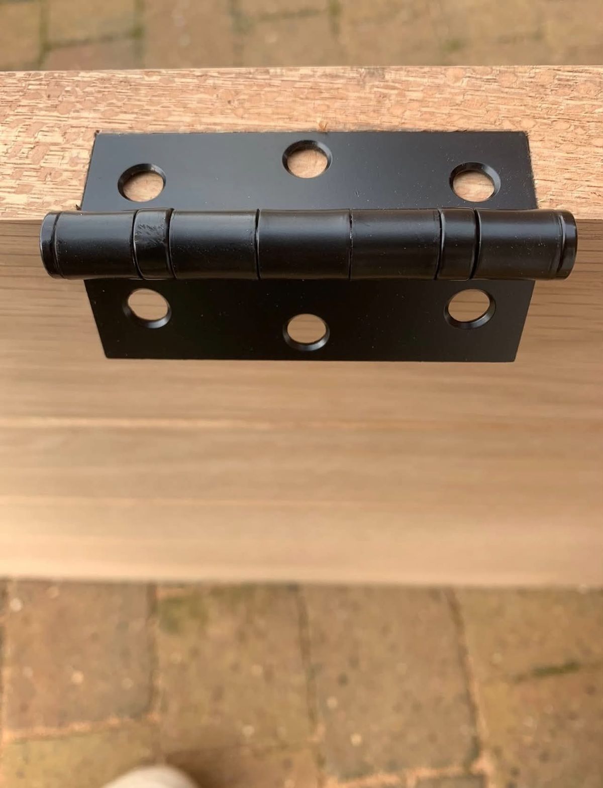 Close-up of a black ball-bearing hinge fitted to the edge of an oak door