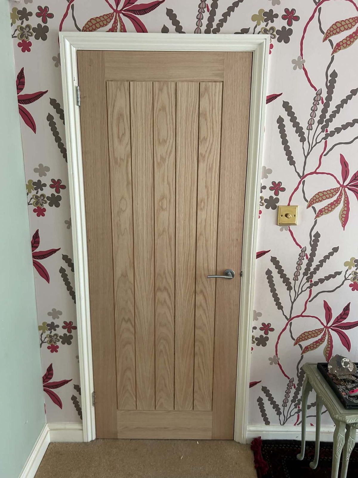 Oak cottage-style internal door with a chrome lever handle against patterned wallpaper