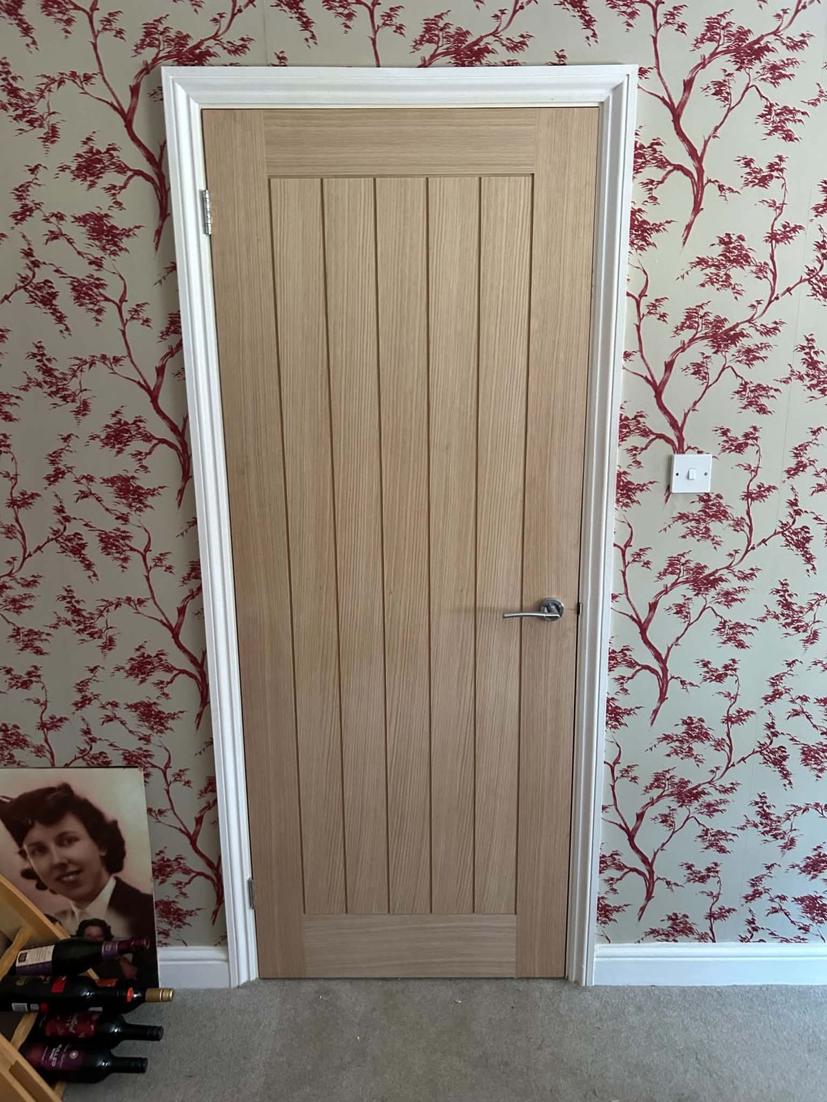 Oak internal door with a chrome handle against red floral wallpaper