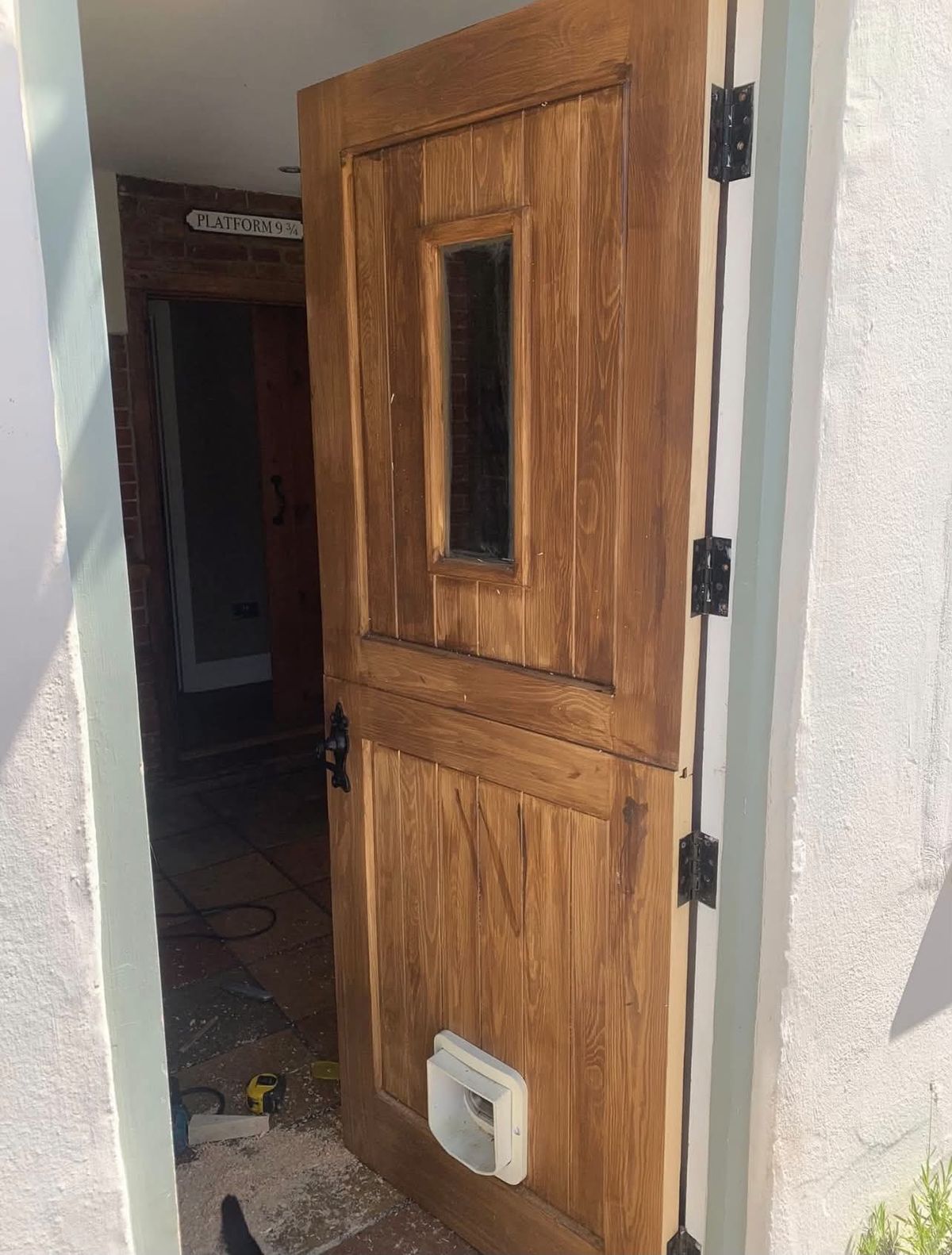 Oak stable door with a glazed top half, black hinges and a pet flap, fitted to a rendered cottage
